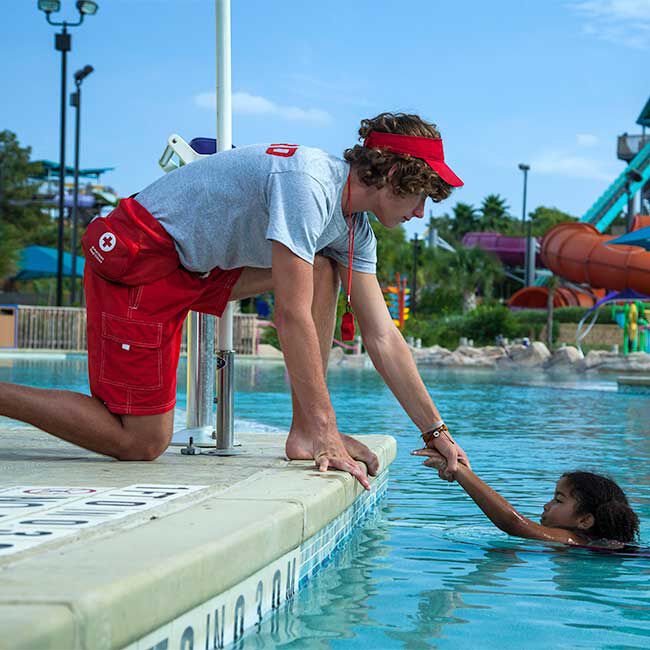 A lifeguard wearing the Red Cross Hip Fanny Pack helping a child get out of the pool.