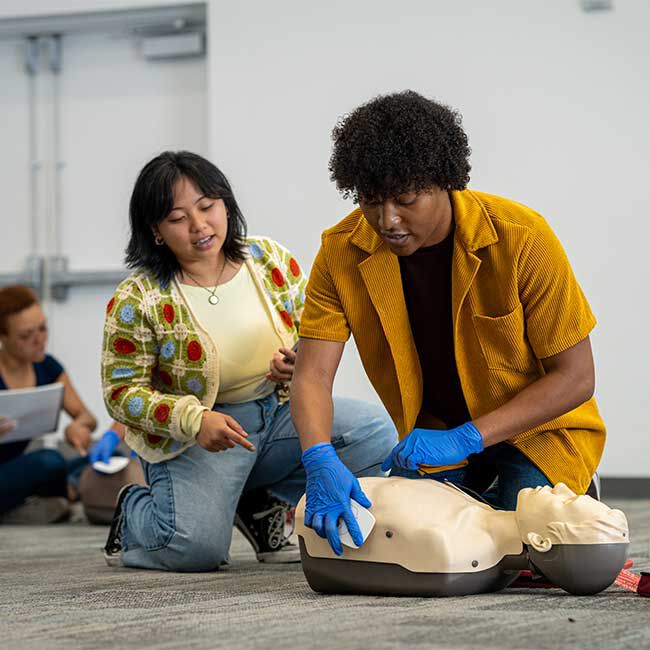 Student applying AED pads to a CPR manikin with an instructor observing the AED pad placement.