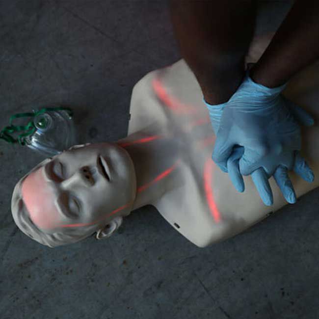 Student wearing blue nitrile gloves practicing CPR compressions on the Brayden/BigRed&trade; Adult CPR Manikin with LED Red Light CPR Feedback.