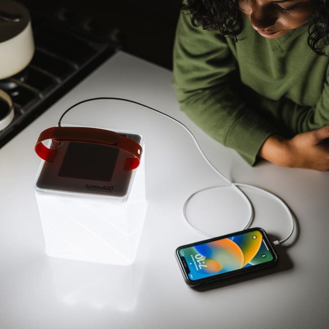 The LuminAID Max QI Lantern illuminated and charging a smartphone.