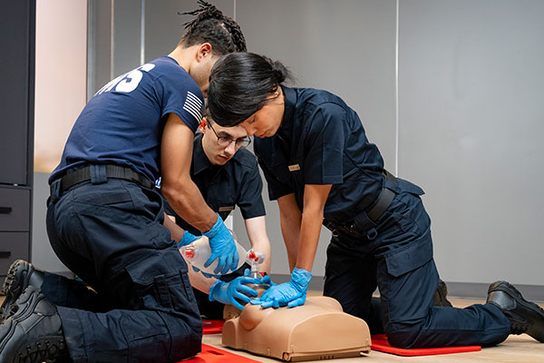 Three New York EMS professionals practicing basic lifesaving skills on a female manikin.