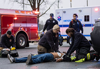 First Responders performing chest compression with AED pads on street.