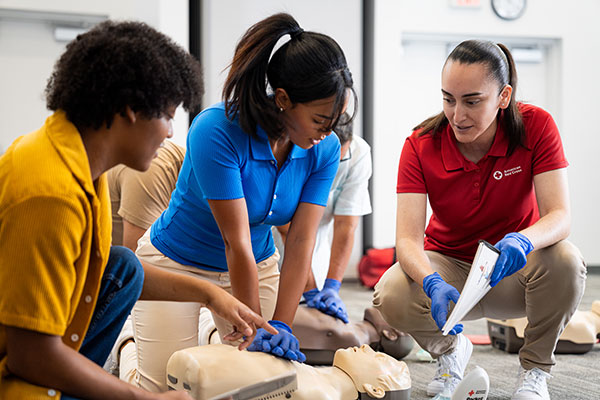 A woman practices performing CPR in Queens, New York while another student watches and the instructor monitors.
