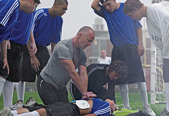Coach demonstrating an AED on a student in front of teammates.