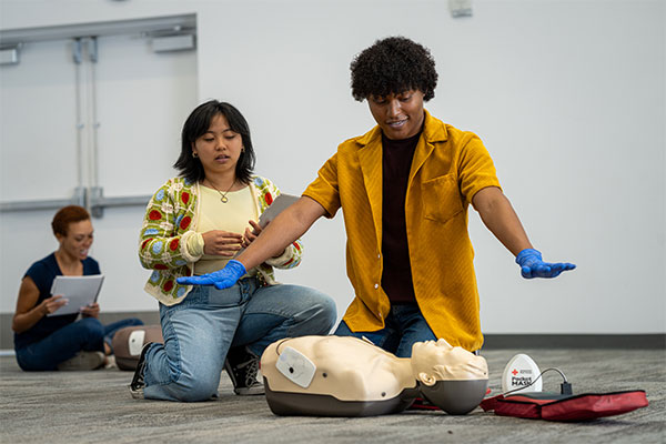 A student practices using an AED on a manikin in Albany, New York demonstrating the clear step with arms spread.