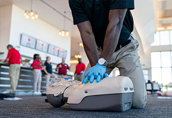 Person performing Hands-Only CPR on CPR manikin in a classroom.